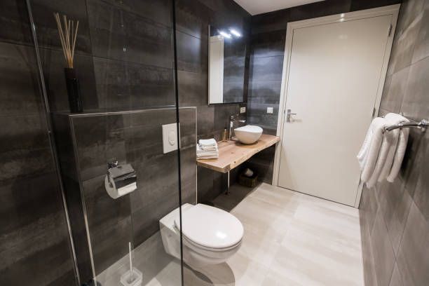 Modern bathroom with glass shower, wall-hung toilet, wood vanity sink, gray tile design.