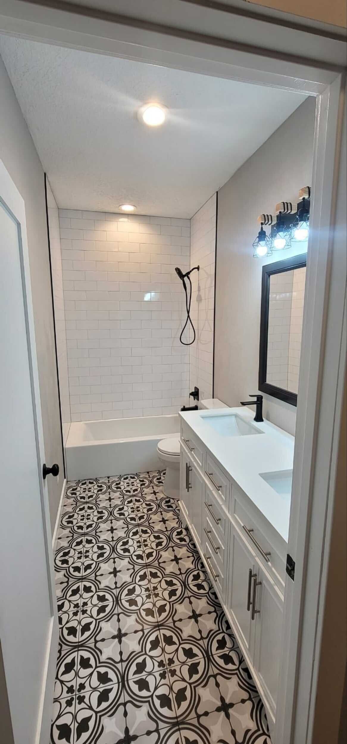Narrow bathroom with patterned tile floor, white vanity, large mirror, and shower at the far end.