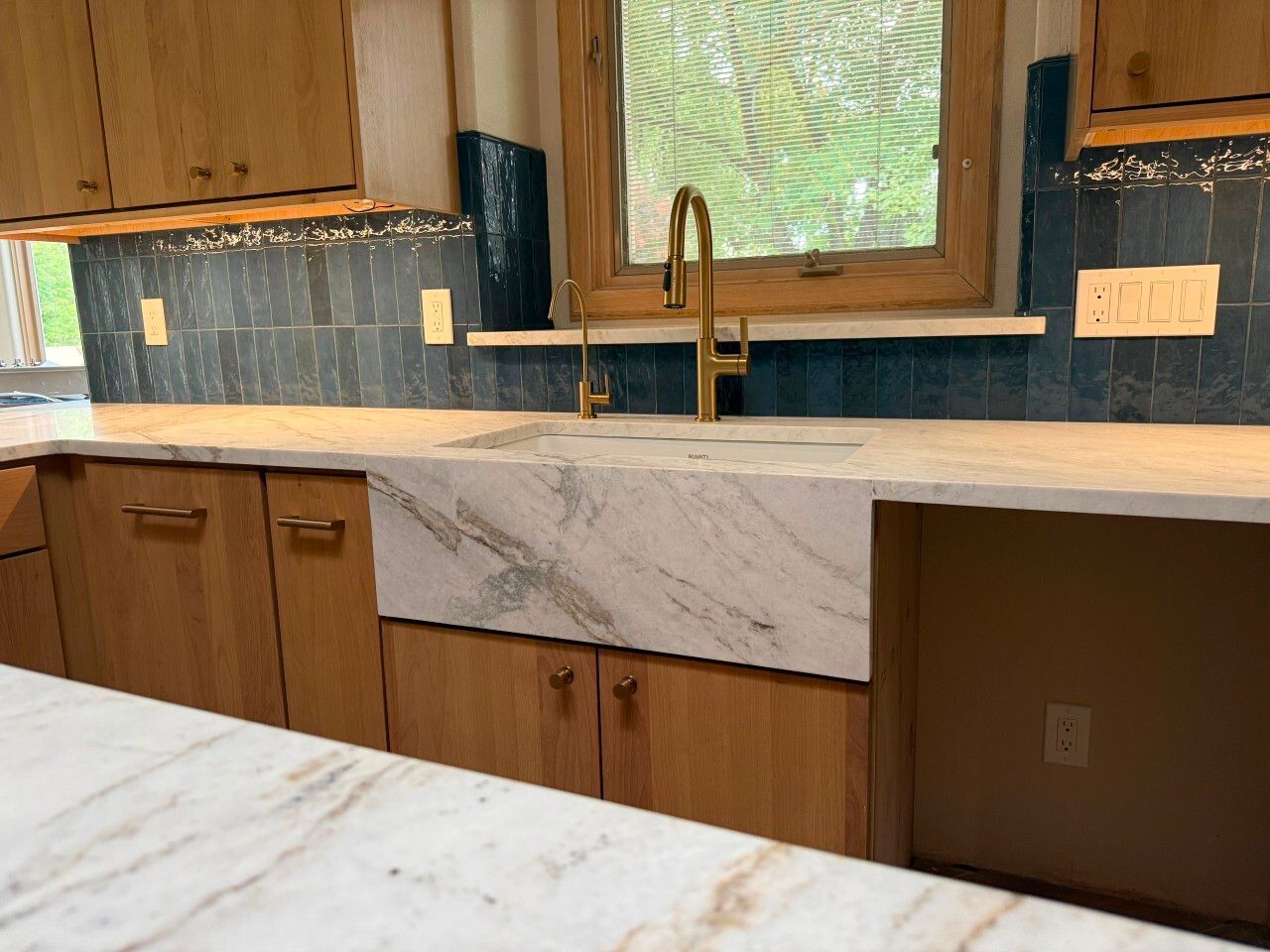 Wood-paneled kitchen with white marble countertops, blue tile backsplash, and a brass faucet by a window.