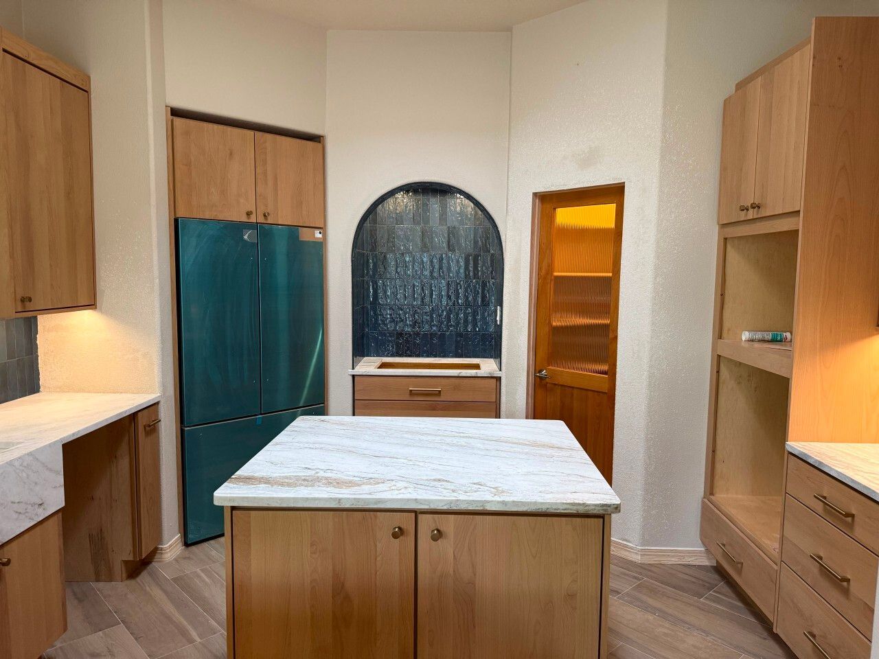Modern kitchen with wood cabinets, white marble island, teal fridge, and arched window backsplash