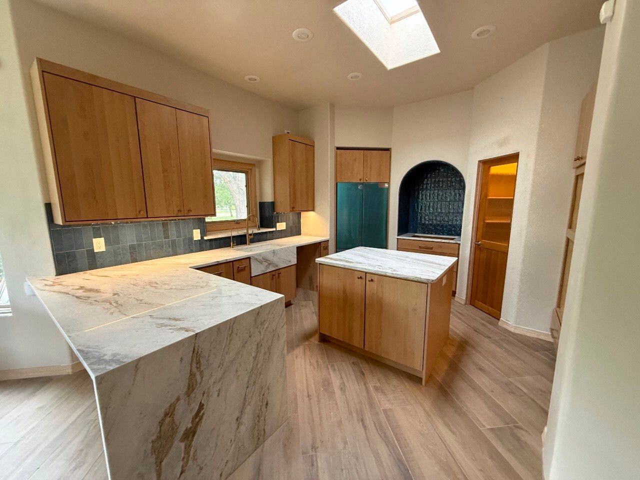 Modern kitchen with wood cabinets, marble island, skylight, and teal refrigerator in a bright open room