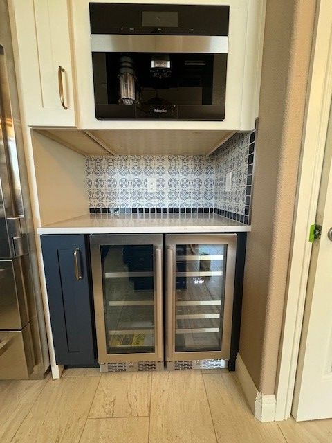 Compact kitchen nook with black microwave, undercounter wine fridge, and patterned backsplash.