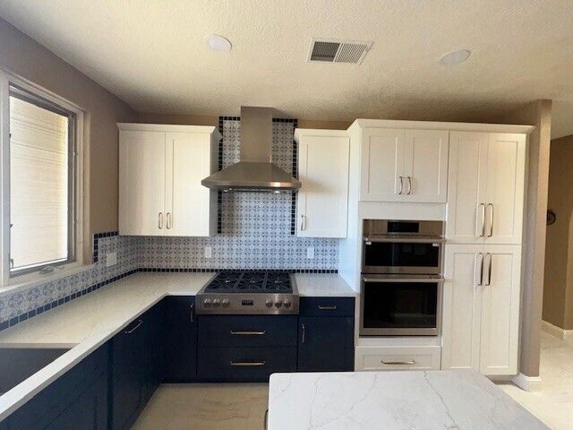 Modern kitchen with white cabinets, dark lower cabinets, stainless range hood, and tiled backsplash