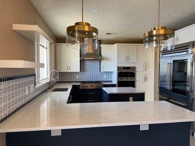 Modern white kitchen with large island, stainless steel appliances, and brass pendant lights.