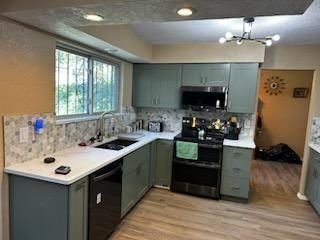 Modern kitchen with mint cabinets, black stove, white countertops, and large window.
