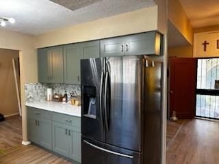 Modern kitchen with teal cabinets, white countertop, and stainless steel refrigerator in an open floor plan.