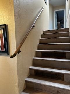 Indoor staircase with beige walls, wooden handrail, and carpeted steps leading to a hallway.