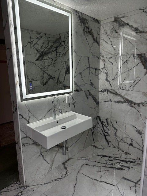Modern bathroom with marble-patterned walls, floating sink, and illuminated mirror panel