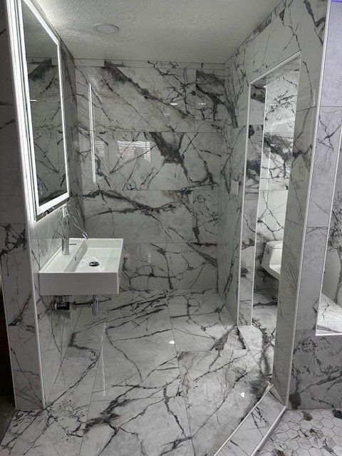 Modern bathroom with marble-pattern tile, sink, mirror, and glass shower stall