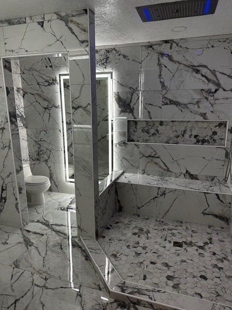 Marble-tiled bathroom with a glass shower door, toilet, and illuminated mirror vanity