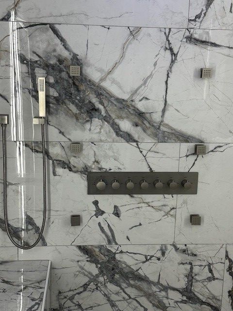 Marble-look tiled wall with shower fixtures, shelf, and plumbing lines in a bathroom under construction