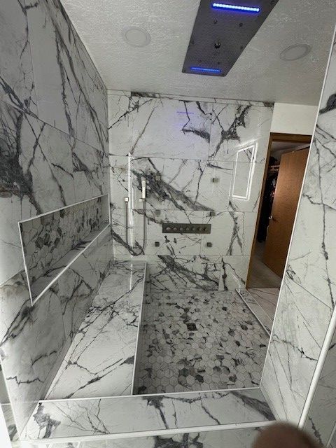 Marble-tiled restroom with a shower bench, grab bars, and a tiled floor