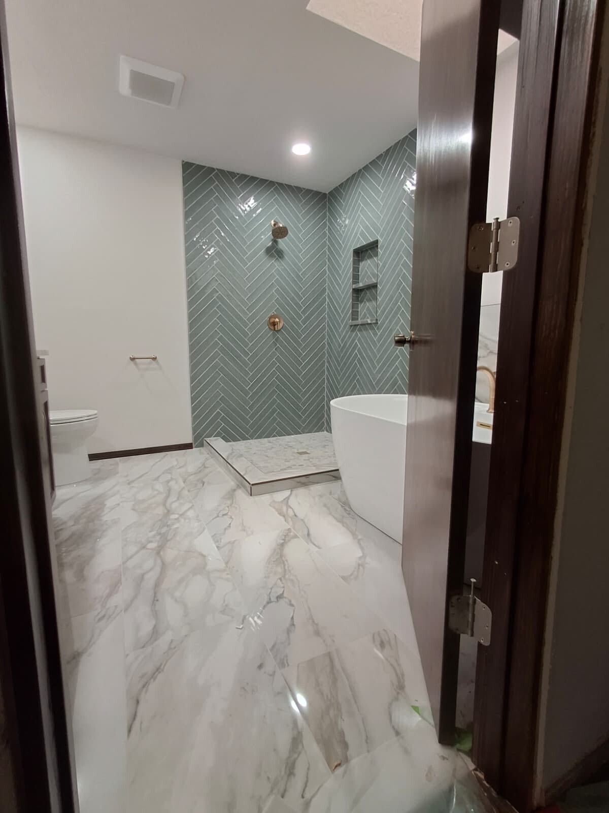 Modern bathroom with marble floor, green patterned shower wall, and a white tub beside a dark doorway