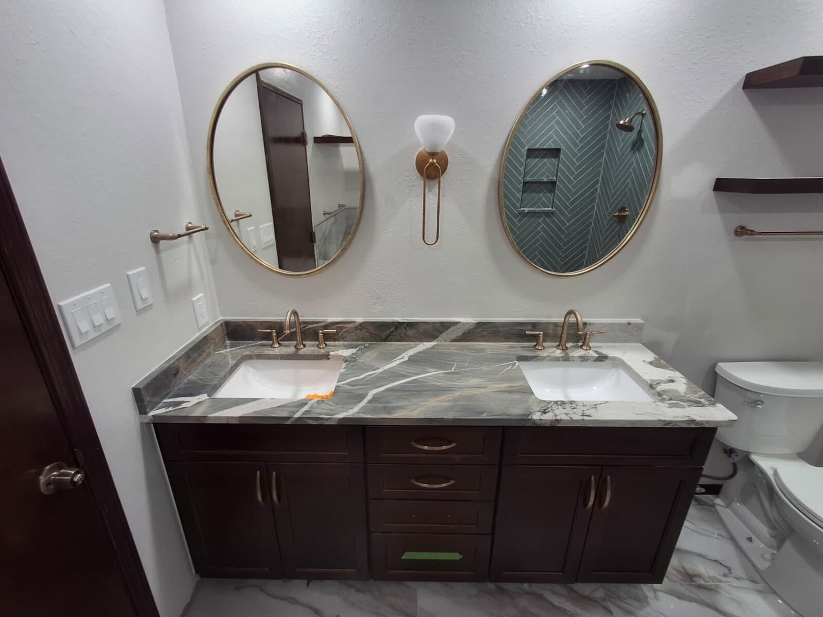 Elegant bathroom vanity with double marble sinks, round mirrors, dark wood cabinets, and wall sconces.