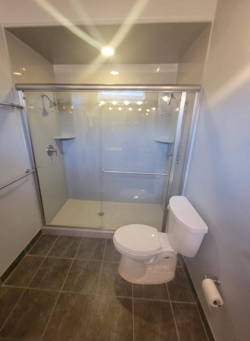 Modern bathroom with glass shower enclosure, toilet, and tiled floor in neutral tones