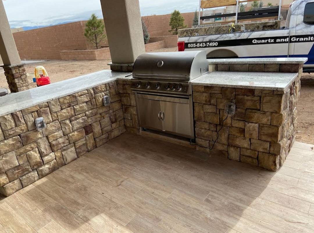 Outdoor stone patio with built-in stainless steel grill and bar counter under a covered patio