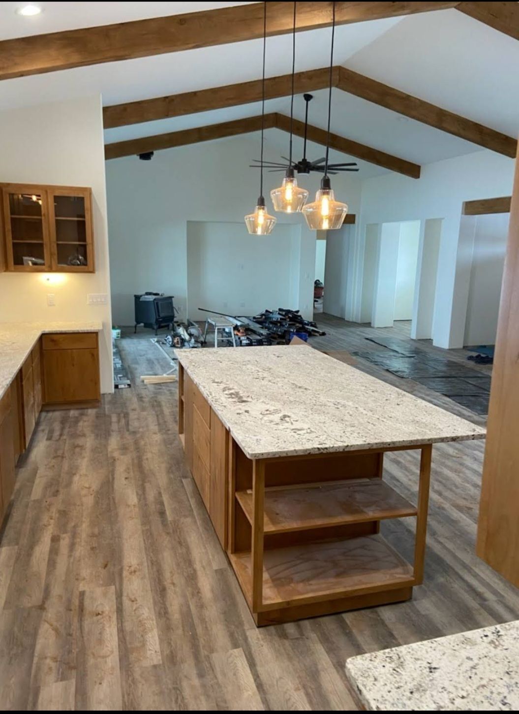 Kitchen with island and hanging lights, open to a living area with wood beams and flooring
