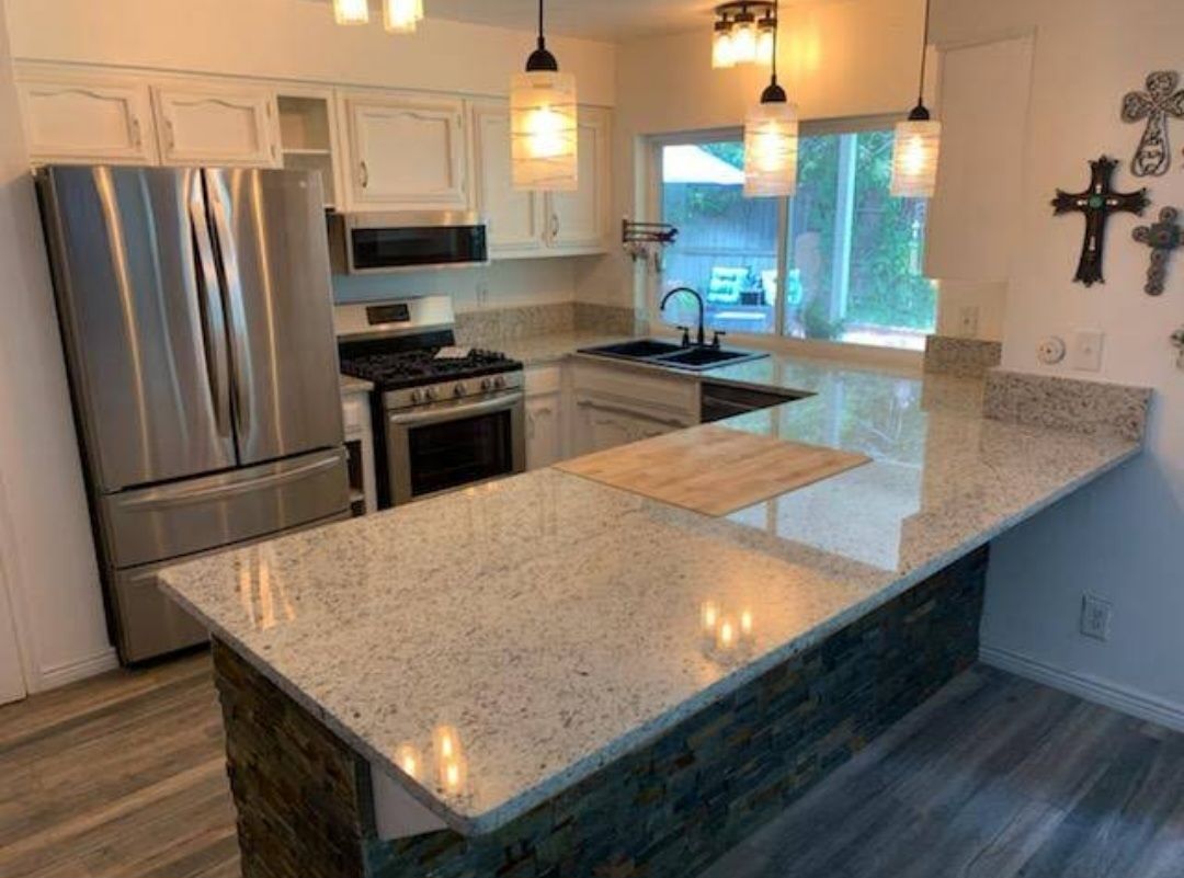 Modern kitchen with stainless appliances, white cabinets, granite island, pendant lights, and a window view
