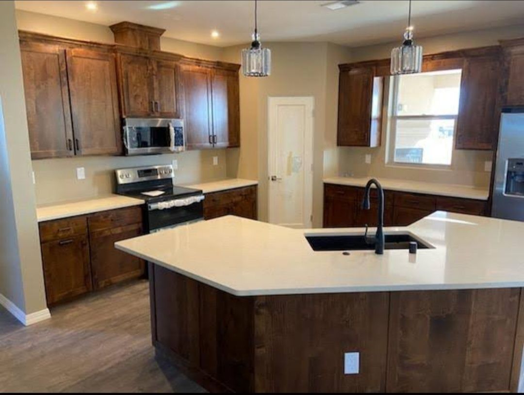 Modern kitchen with dark wood cabinets, large island, pendant lights, and stainless steel appliances