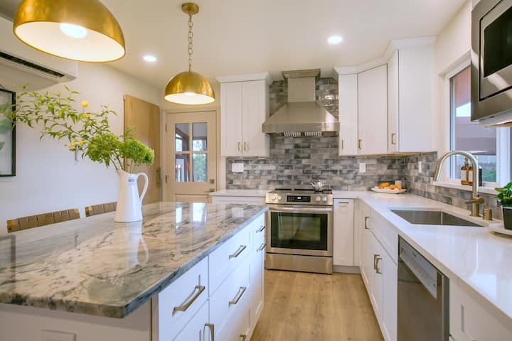 Bright modern kitchen with marble island, white cabinets, gold pendant lights, and stainless steel appliances