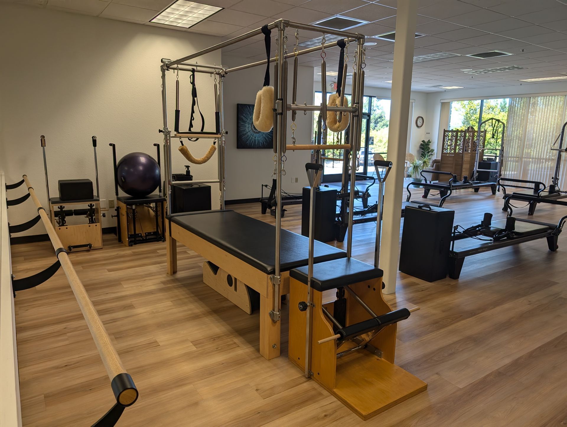 Pilates studio with exercise equipment. Reformer bed, tower, and other apparatuses on wood floor.
