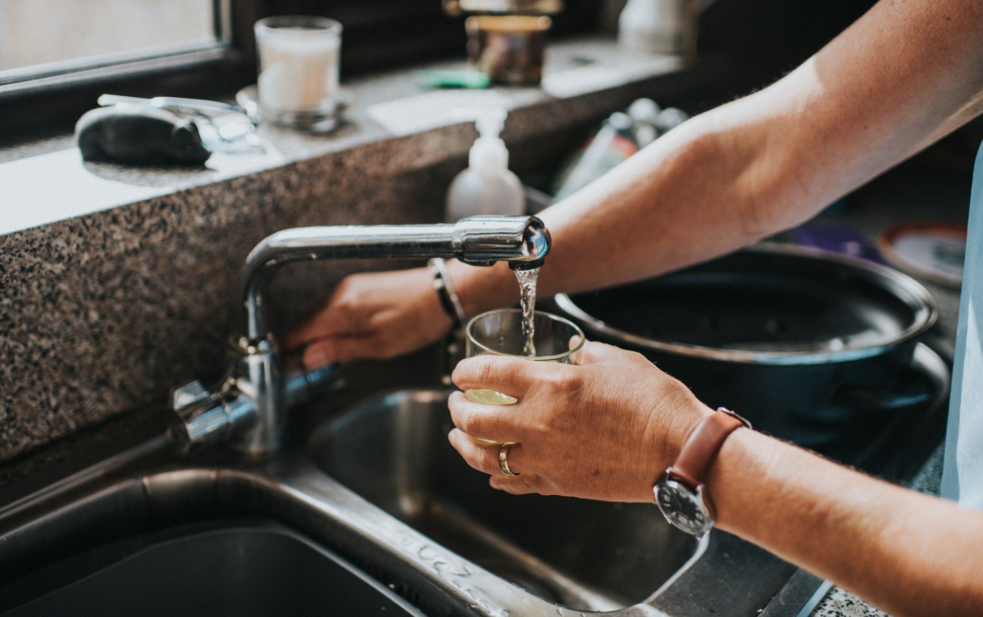 Person filling a glass with water from a kitchen sink faucet.