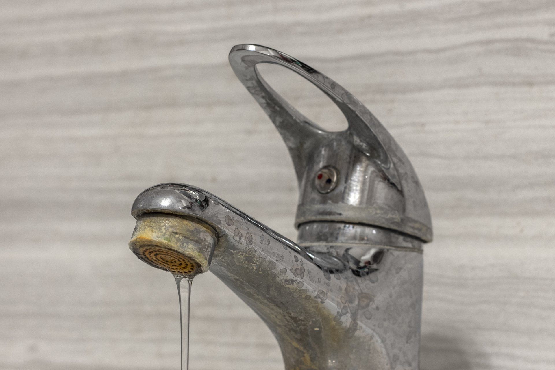 Hard Water — Muncie, IN — Oxley Softwater Co. Close-up of a chrome faucet with mineral deposits, dripping water, set against a light, patterned wall.