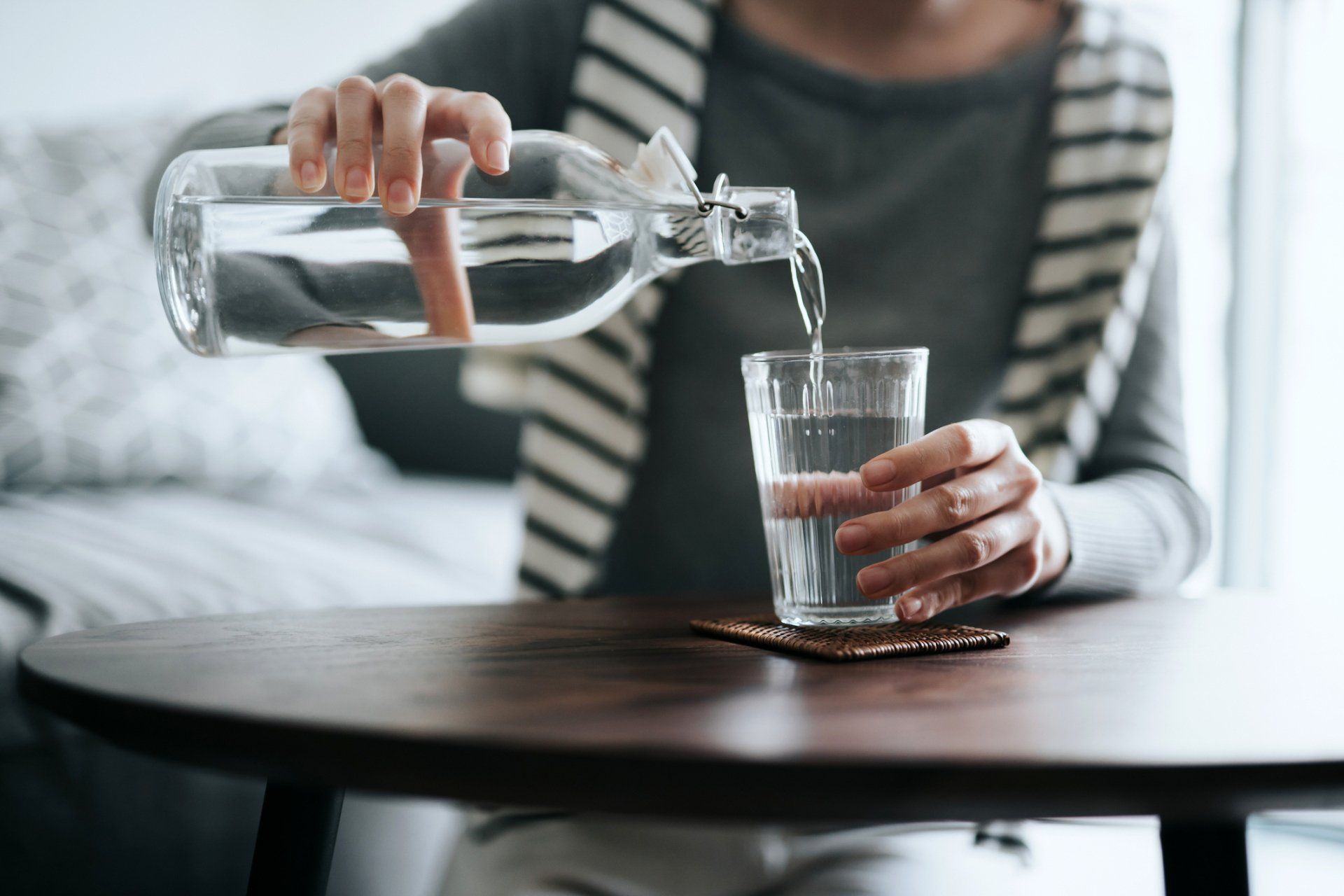 Transferring Water — Muncie, IN — Oxley Softwater Co. Person pouring water from a glass bottle into a glass on a wooden table.