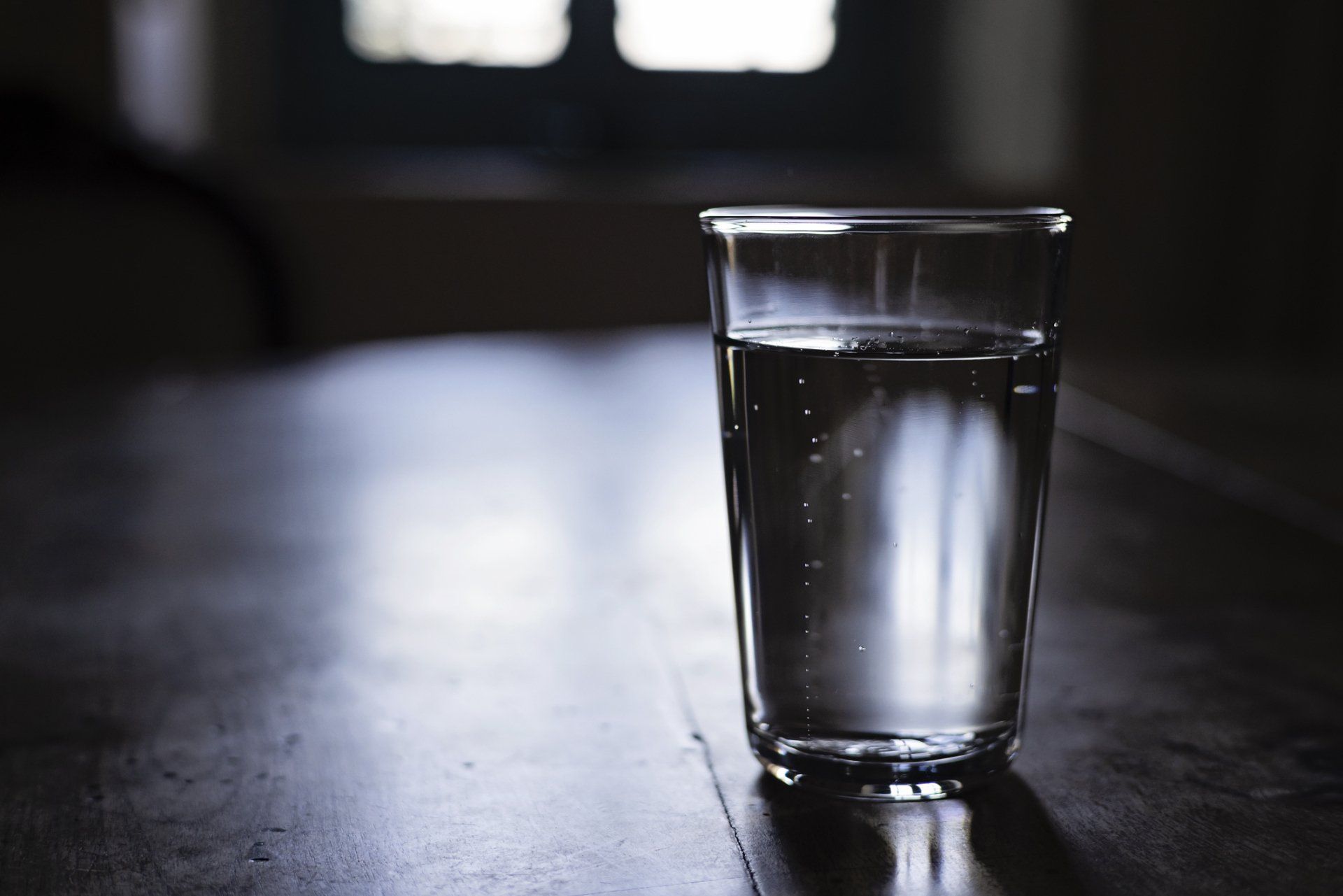 Cloudy Water — Muncie, IN — Oxley Softwater Co. Glass of water on a dark wooden table, with a blurred window in the background.