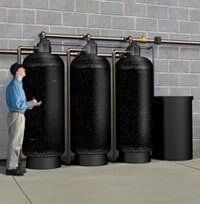 Water Tanks — Muncie, IN — Oxley Softwater Co. Man looking up at three large black water filtration tanks in a utility room.