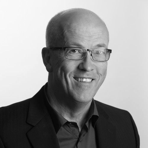 Black-and-white portrait of a smiling bald man wearing glasses and a dark suit jacket