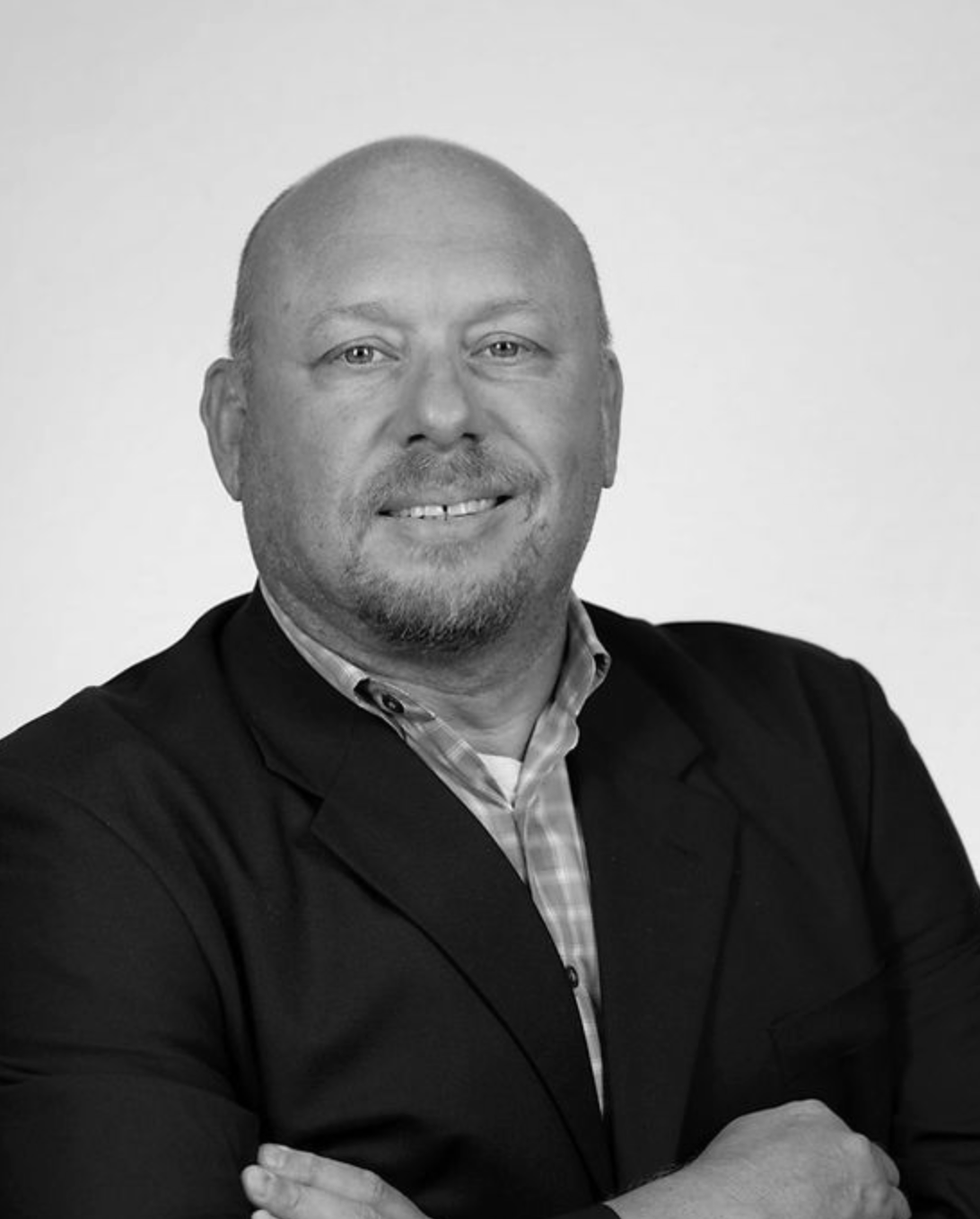 Portrait of a bald man in a dark suit jacket, smiling against a plain light background