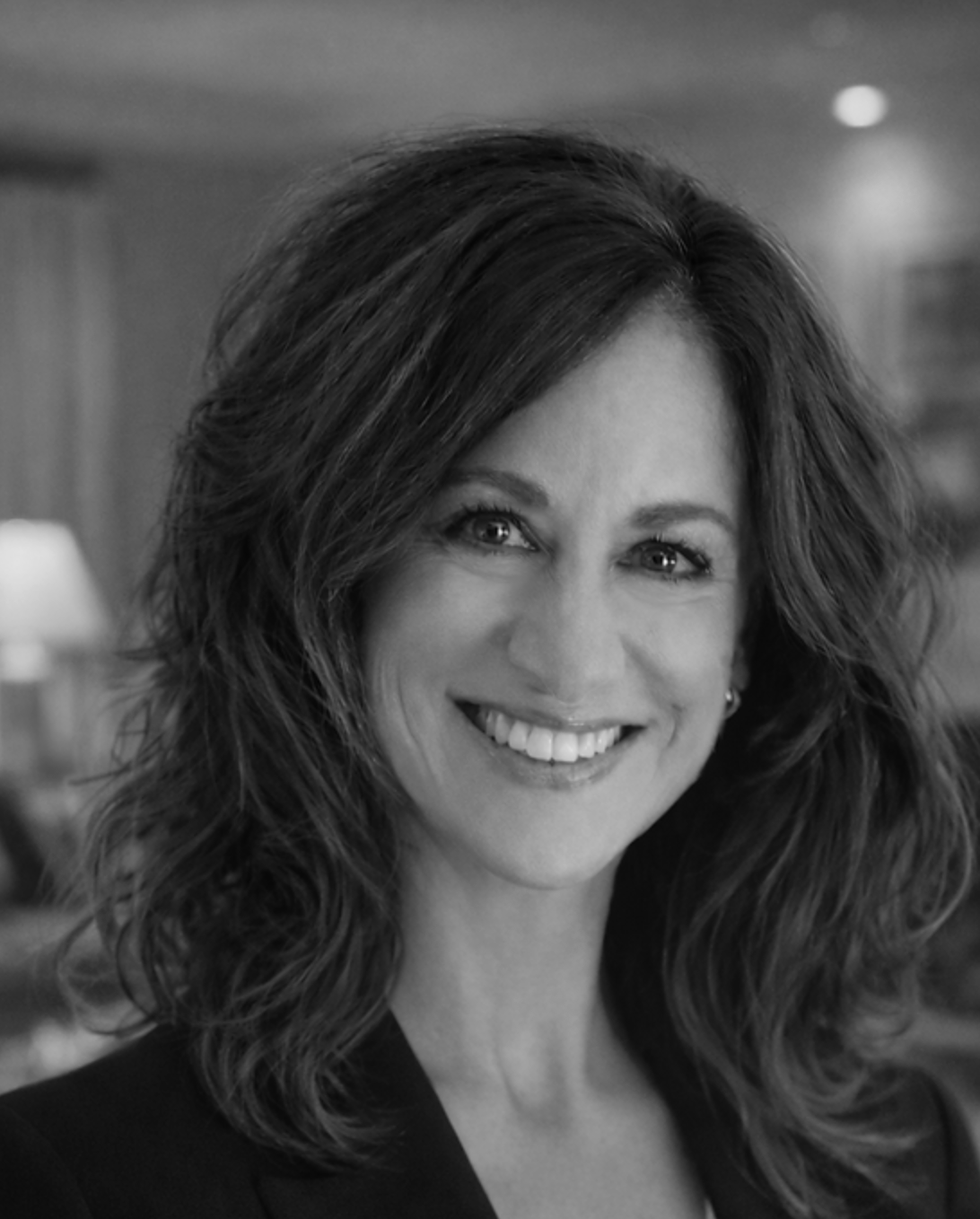 Black-and-white portrait of a smiling woman with wavy dark hair in a softly lit indoor setting