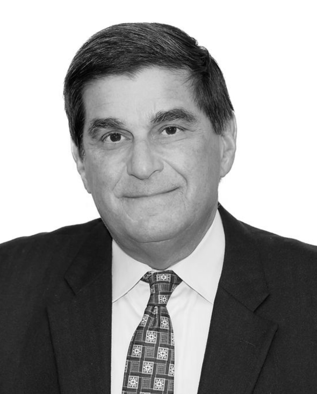 Studio headshot of a man in a dark suit, white shirt, and patterned tie against a plain background