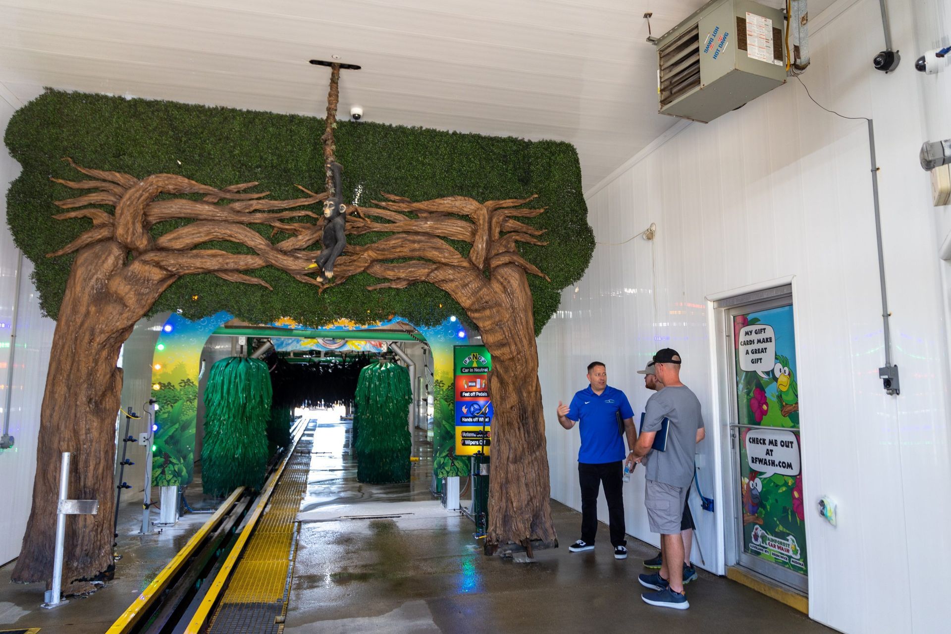Three men are standing in a car wash with a tree in the background.
