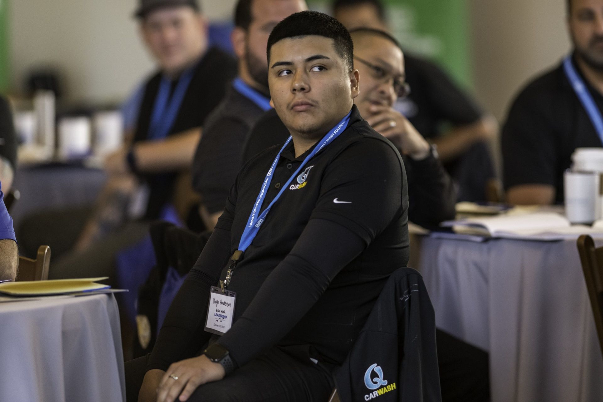 A man is sitting at a table with a lanyard around his neck.