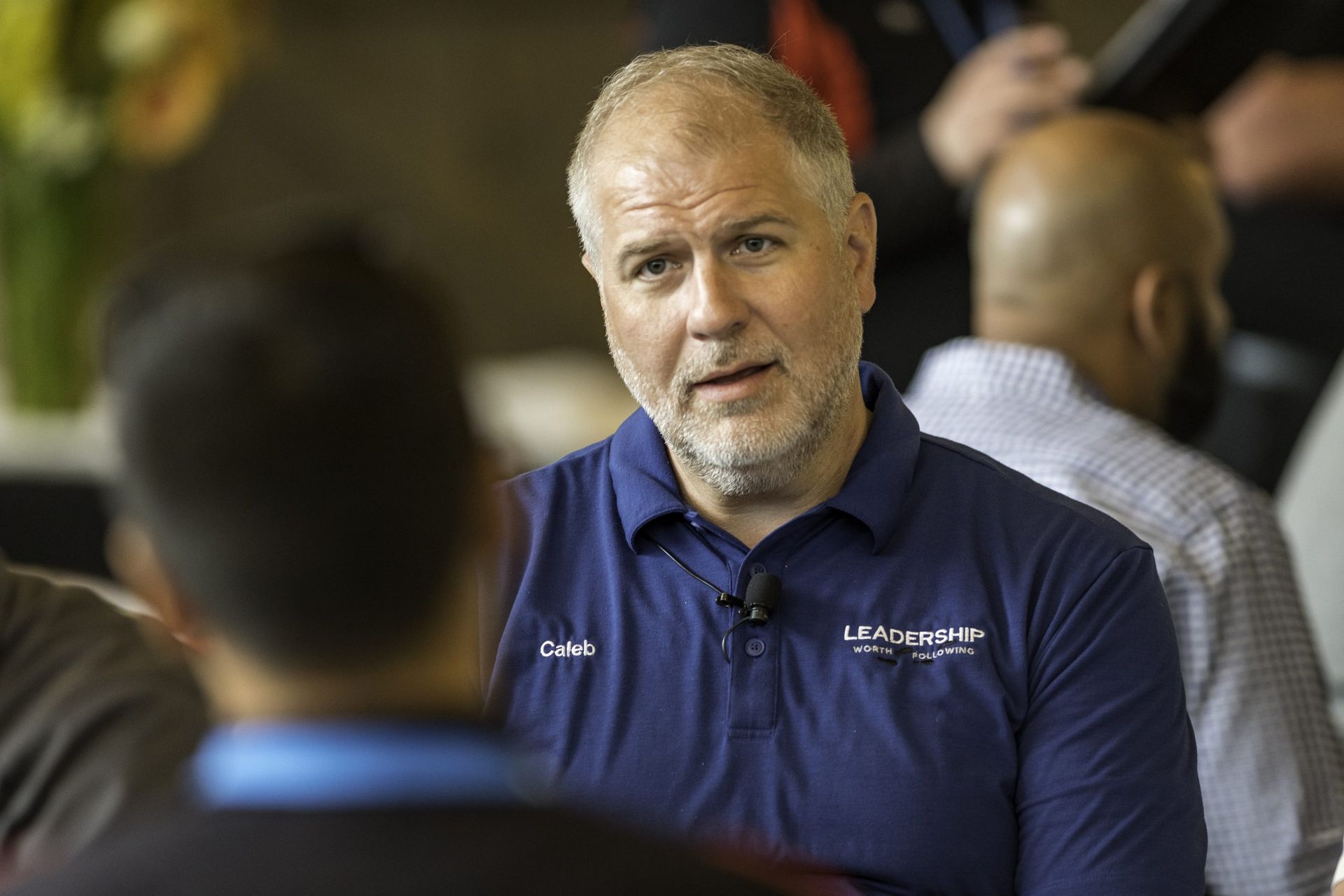 A man with a beard is talking to another man in a blue shirt.