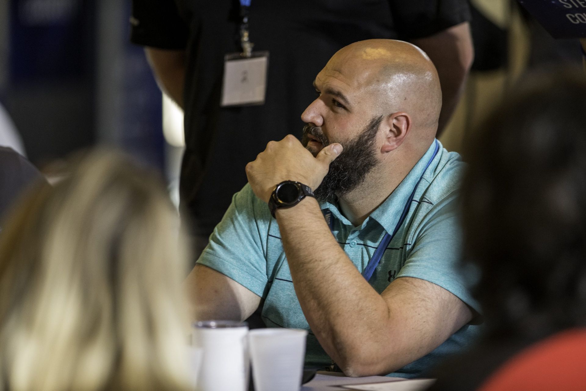 A bald man with a beard is sitting at a table with other people.