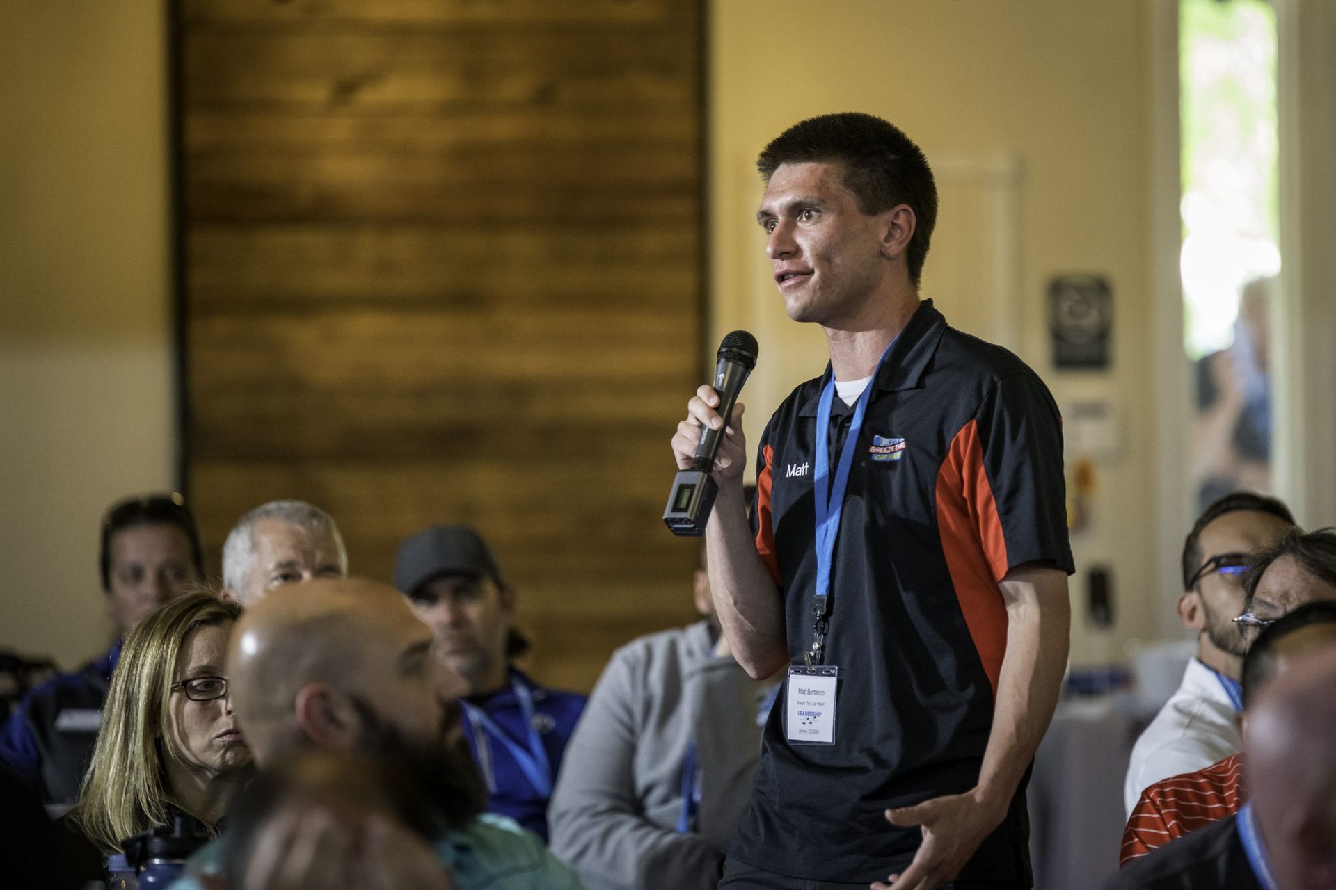 A man is holding a microphone and talking to a group of people.