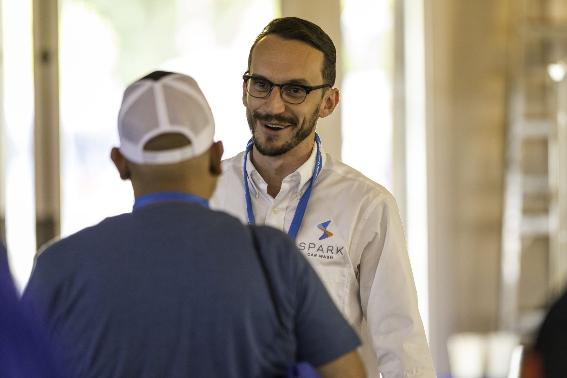 A man in a white shirt is talking to another man in a blue shirt.