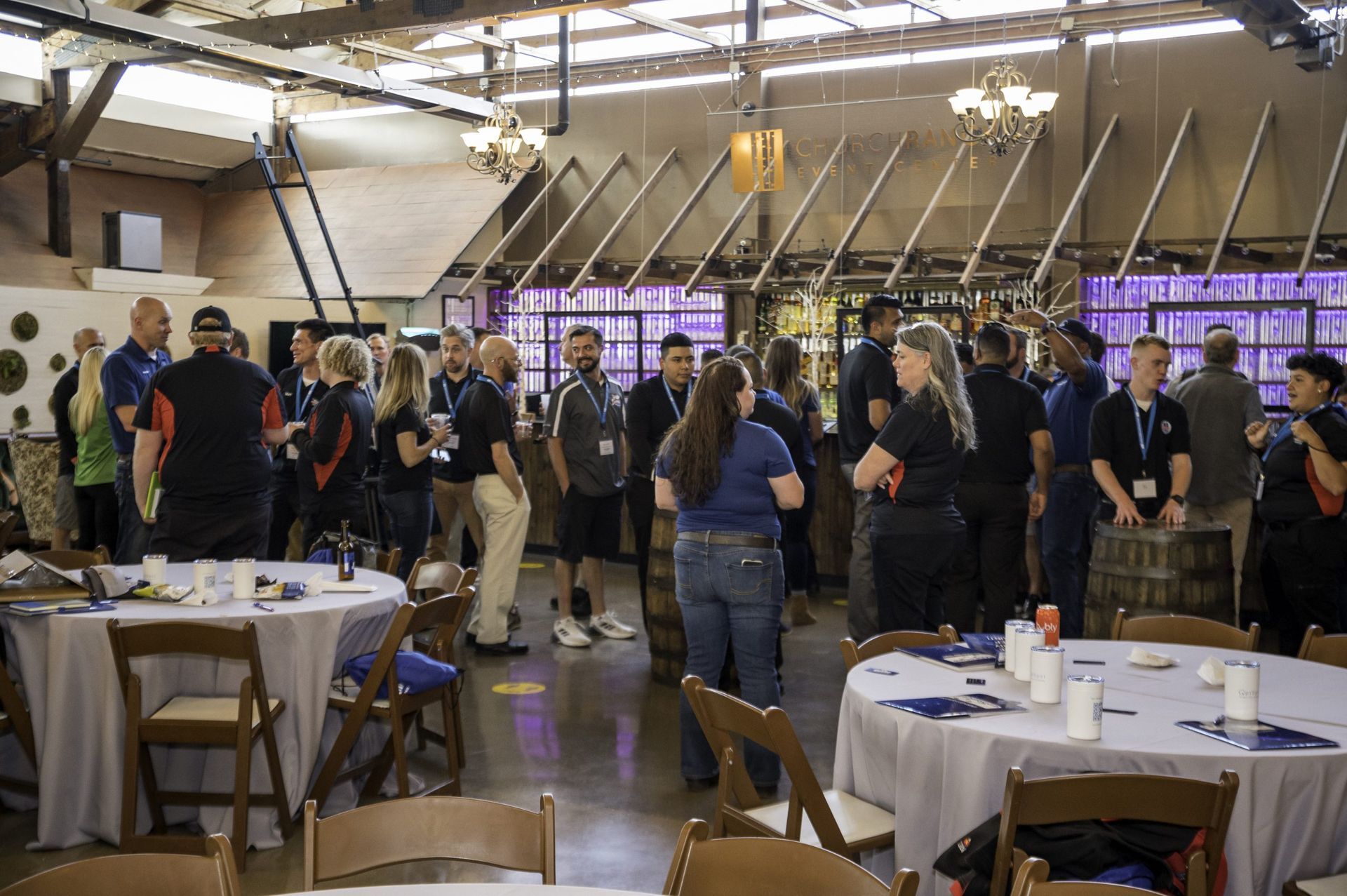 A group of people are standing around tables and chairs in a room.