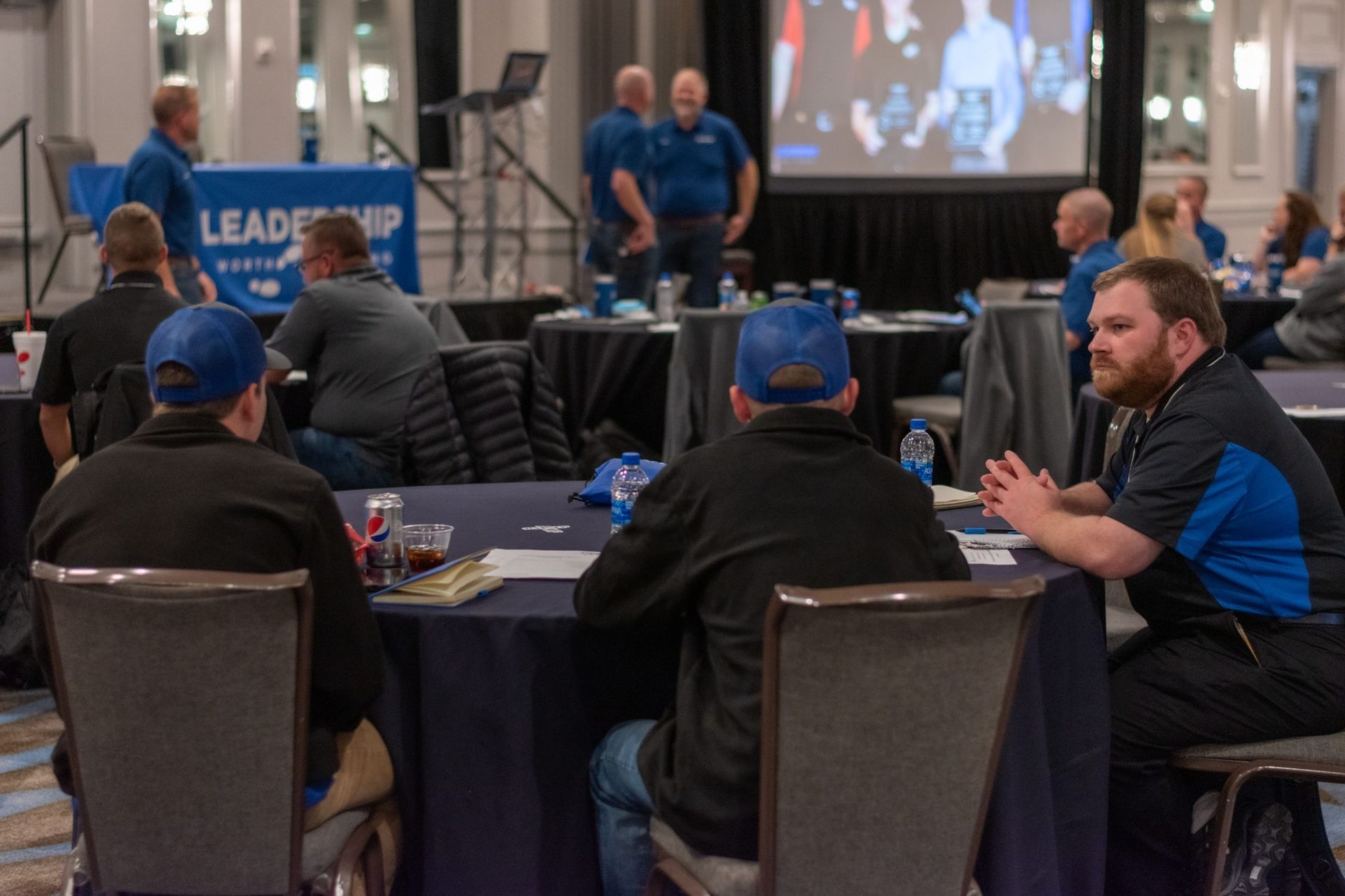 A group of men are sitting at tables in a conference room.