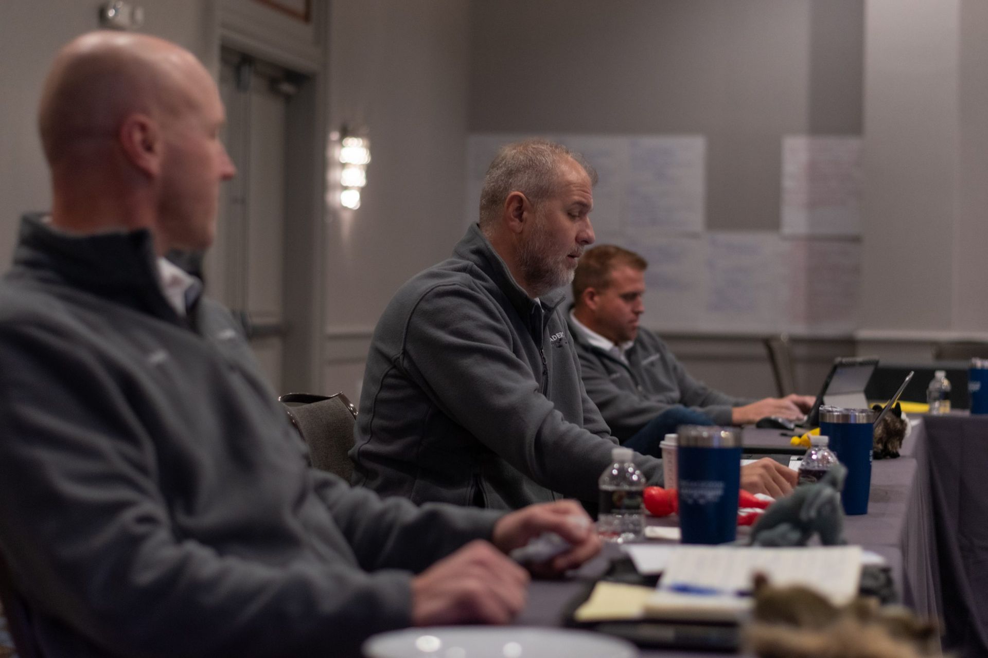 A group of men are sitting at a table with laptops.