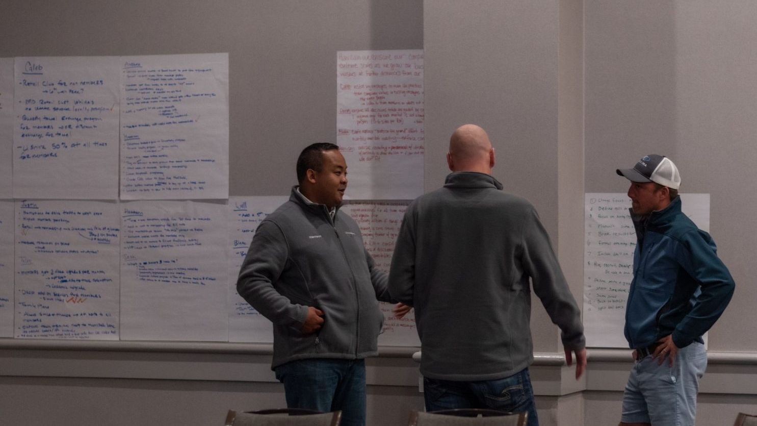 Three men are standing in front of a whiteboard in a room.