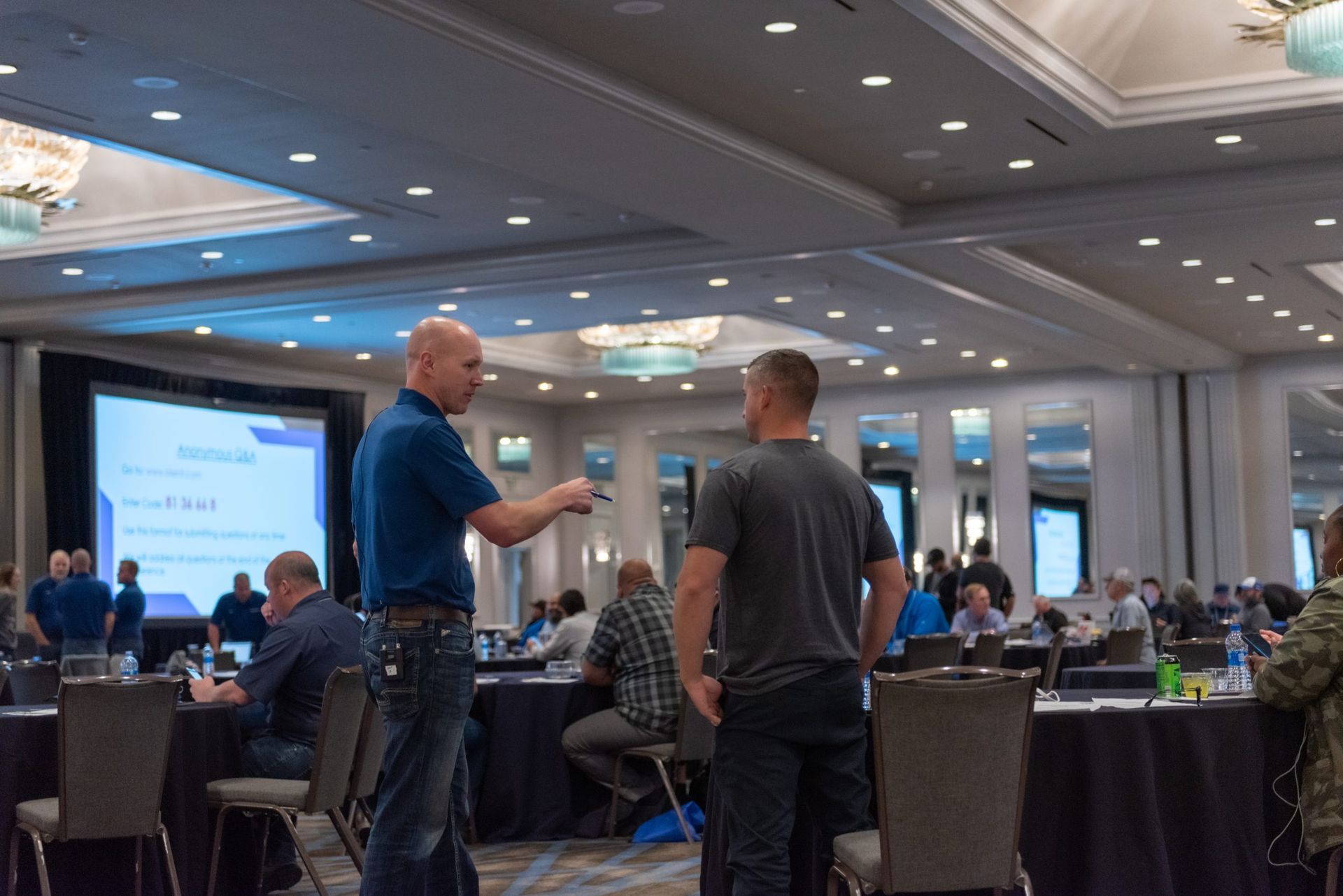 A group of men are standing in a large room talking to each other.