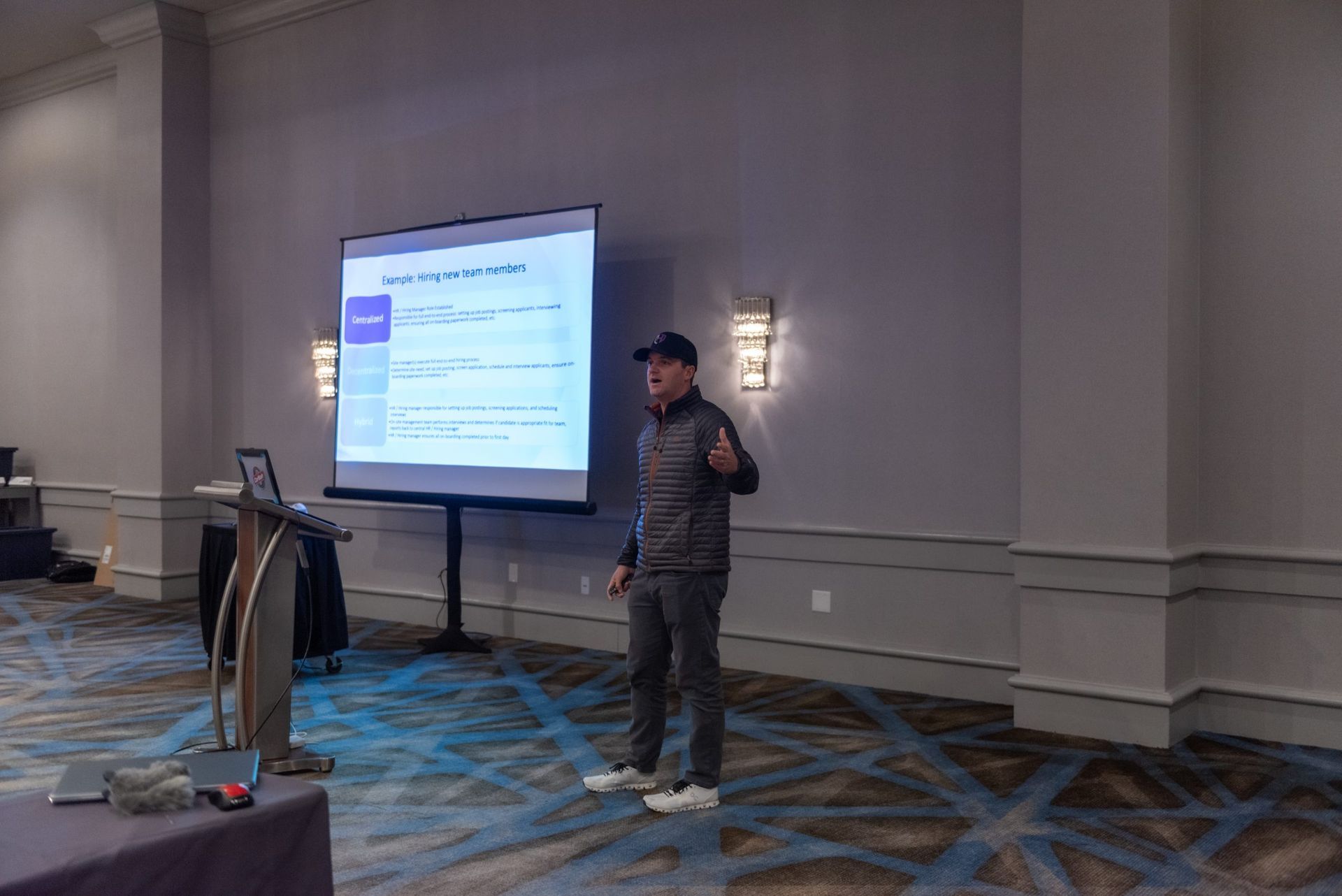 A man is giving a presentation in front of a large screen in a conference room.
