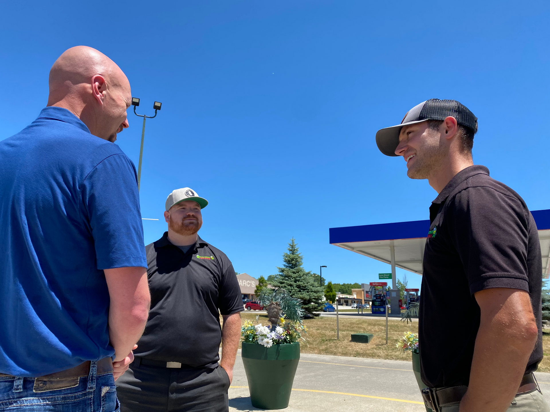 Three men are standing in front of a gas station talking to each other.