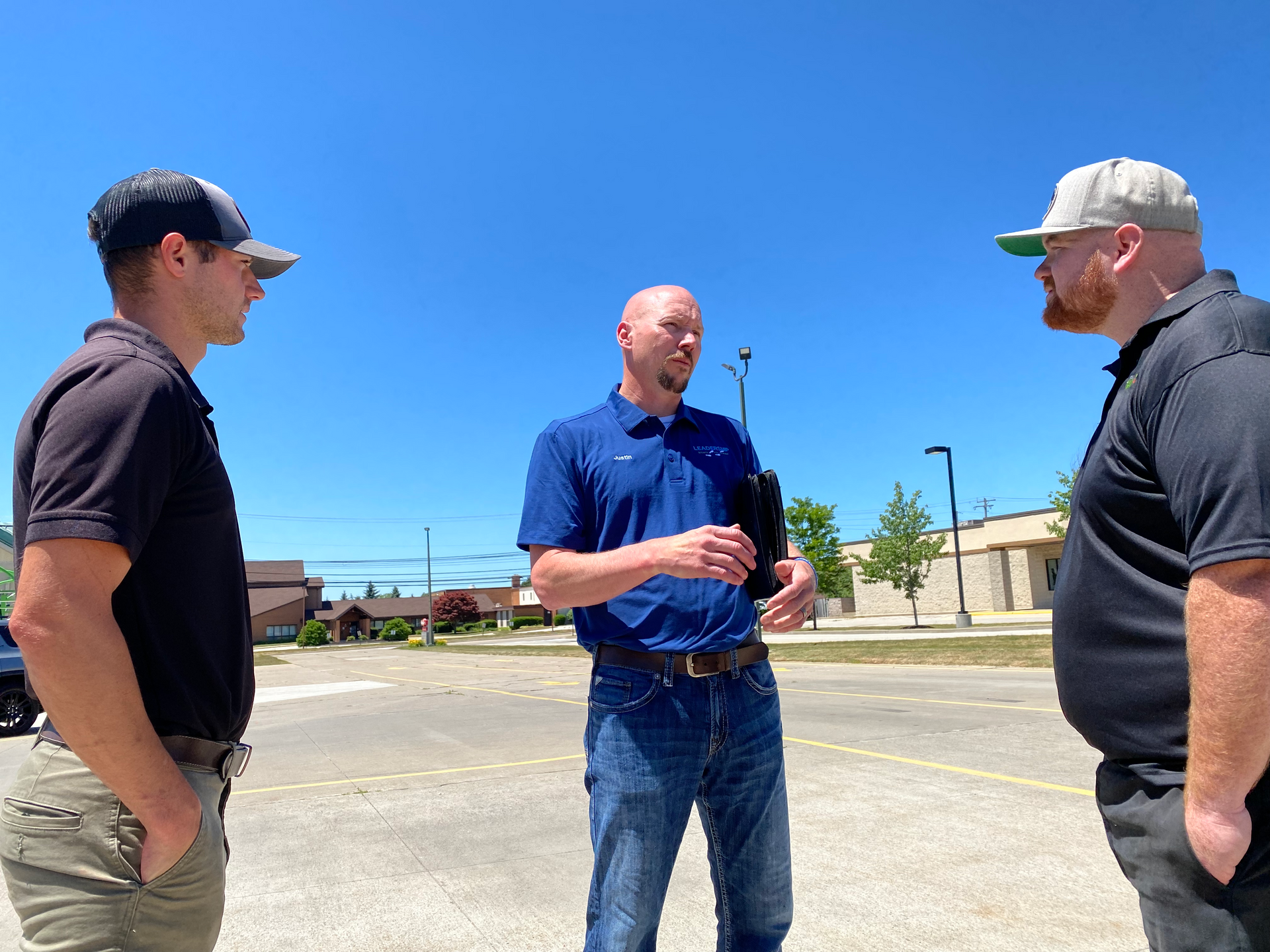 Three men are standing in a parking lot talking to each other.