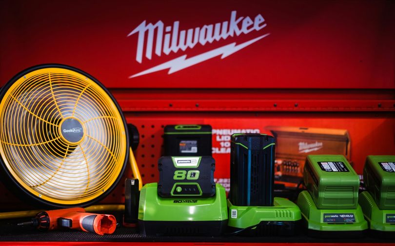 Milwaukee tool display with yellow fan, batteries, charger, and red tool chest background