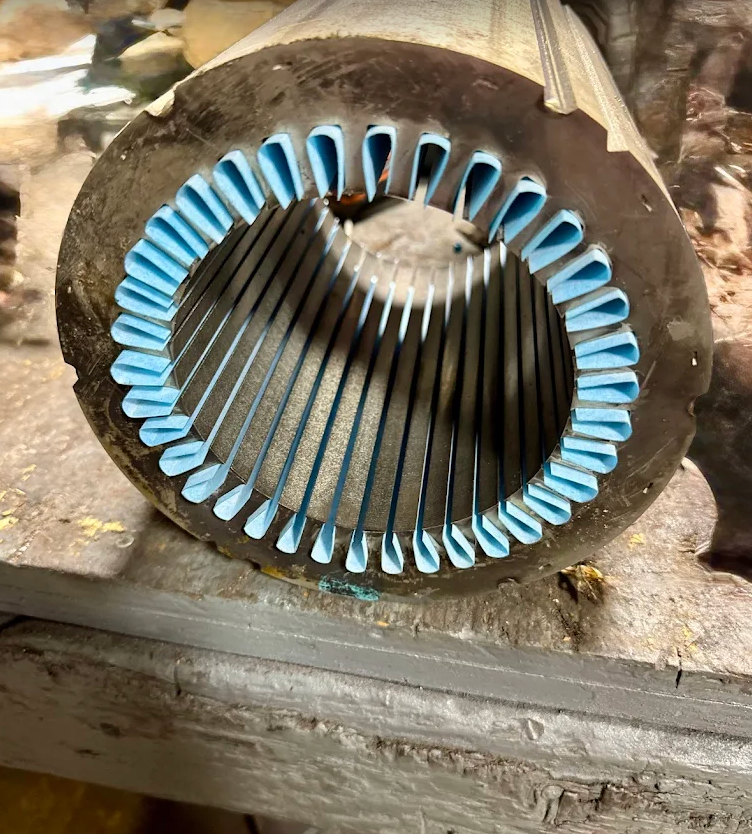 Circular motor stator with blue coil windings on a workbench, viewed end-on